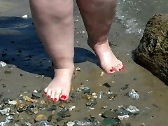 piernas desnudas y gordas con pedicura roja camina a lo largo de la orilla del río, fetiche