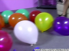 Nikita blowing up balloons and popping them topless